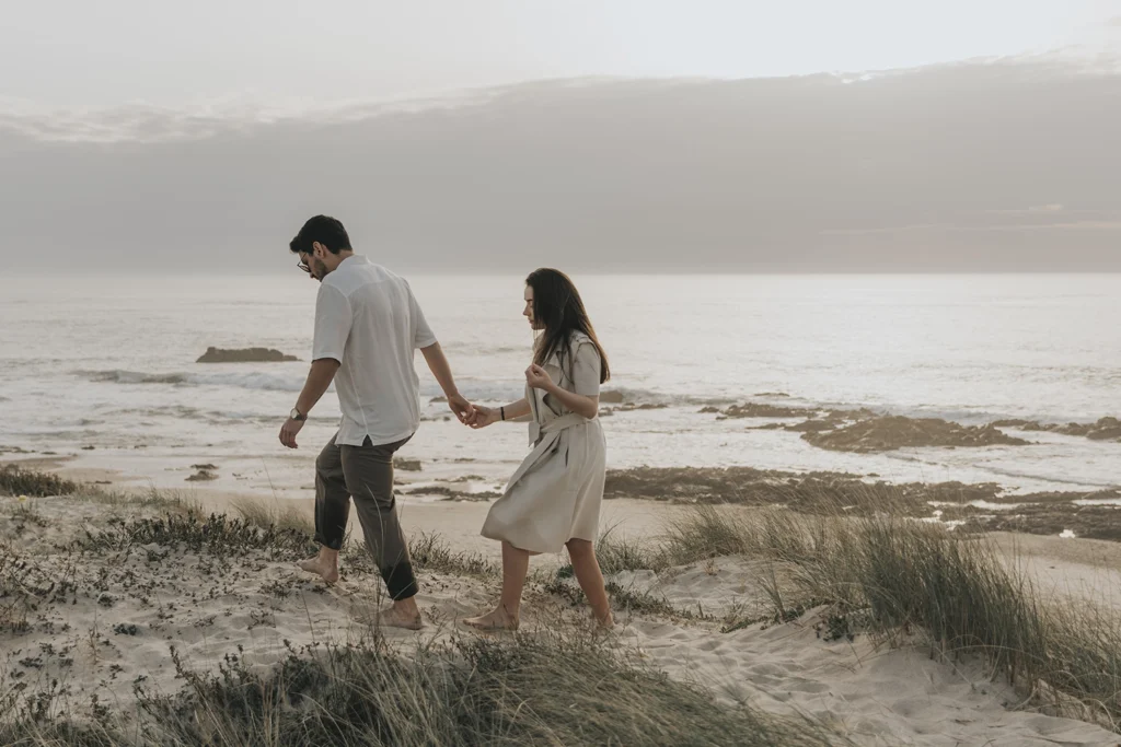 Casal nas dunas, caminhando com o horizonte em plano de fundo, envolvido pela paisagem.