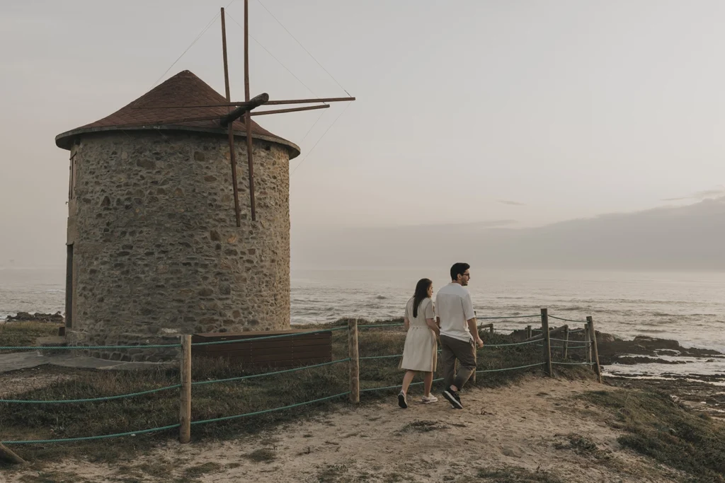 Casal caminha junto a um moinho de vento, com o horizonte em plano de fundo.