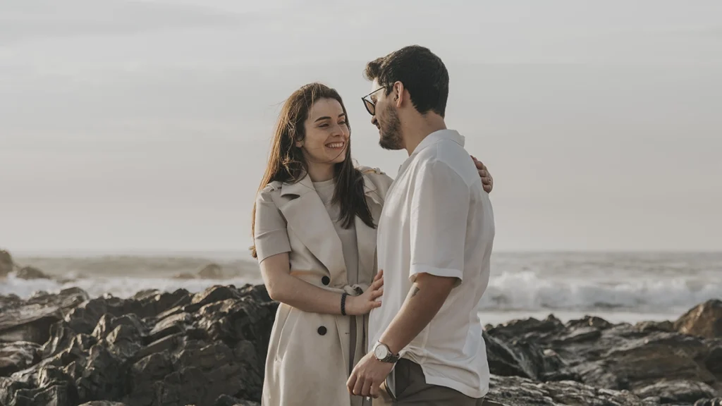 Casal troca um olhar apaixonado na praia, capturando um momento de amor e conexão à beira-mar.