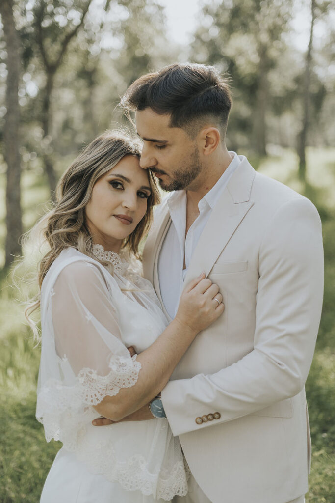 Casal abraçado no bosque, em pose romântica, durante o dia do casamento, rodeado pela natureza e tranquilidade.