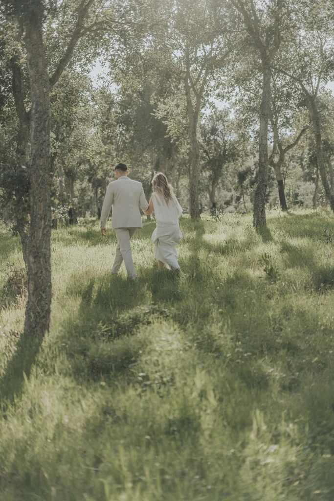 Casal caminhando juntos pelo bosque, mãos dadas, imersos na natureza no dia do casamento.