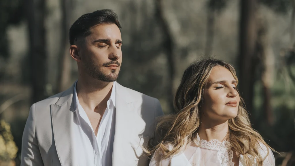 Casal com os olhos fechados, em um momento de reflexão e introspecção, capturado no dia do casamento em um cenário sereno e natural.